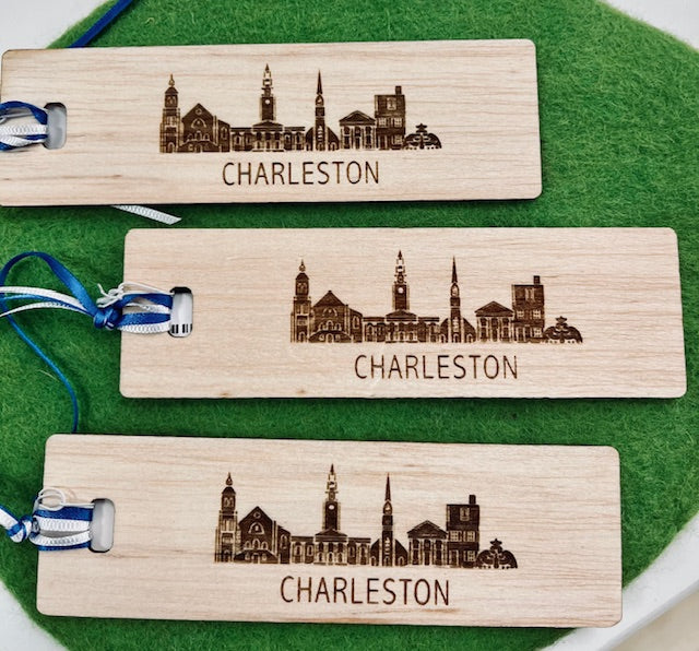 Three bamboo bookmarks with the Charleston skyline engraved on them, displayed on a green surface.