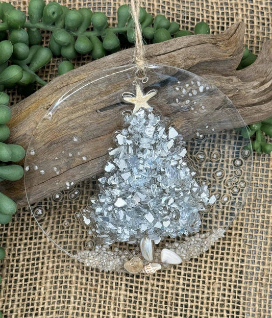 A silver crushed glass Christmas tree ornament with seashells and a starfish on a sandy beach, set in resin, with a twine hanger.