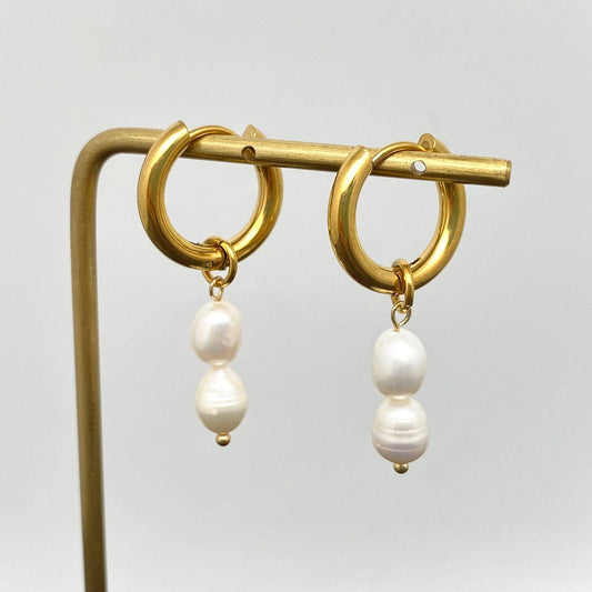 Gold hoop earrings with pearl drops on a stand against a light gray background